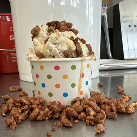 Ice cream sundae topped with candied walnuts spilling over the cup