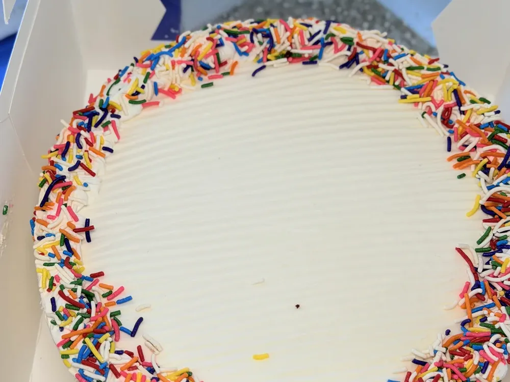 Round homemade ice cream cake with a rainbow sprinkle border, boxed at Ryan's