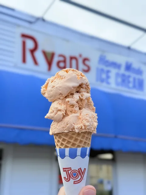 Double scoop of Jersey peach ice cream on a cone in front of Ryan's