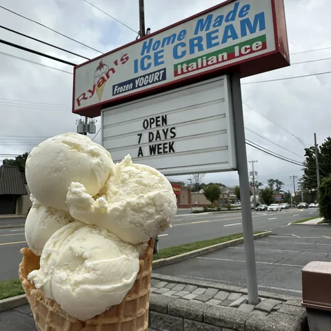 Triple scoop vanilla ice cream cone in front of the Ryan's Homemade Ice Cream roadside sign